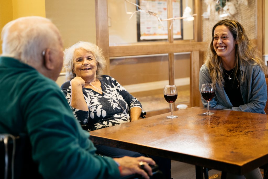 3 people at a table drinking wine together and smiling