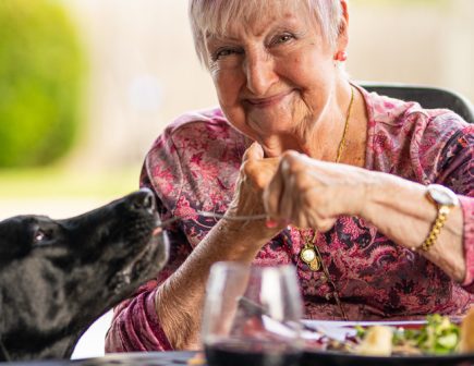 elderly woman eating dinner with dog